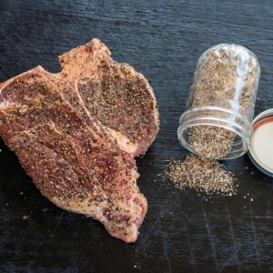 steak rub jar spilled next to seasoned porterhouse steak