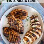 grilled chicken breasts on a plate. One is sliced.