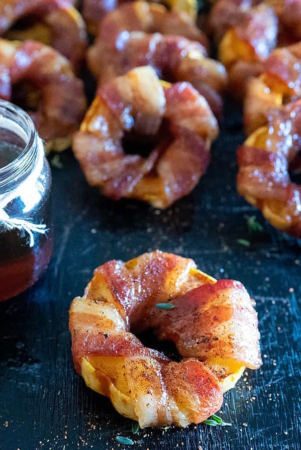 Bacon Wrapped Grilled Delicata Squash Rings on platter by jar of syrup.