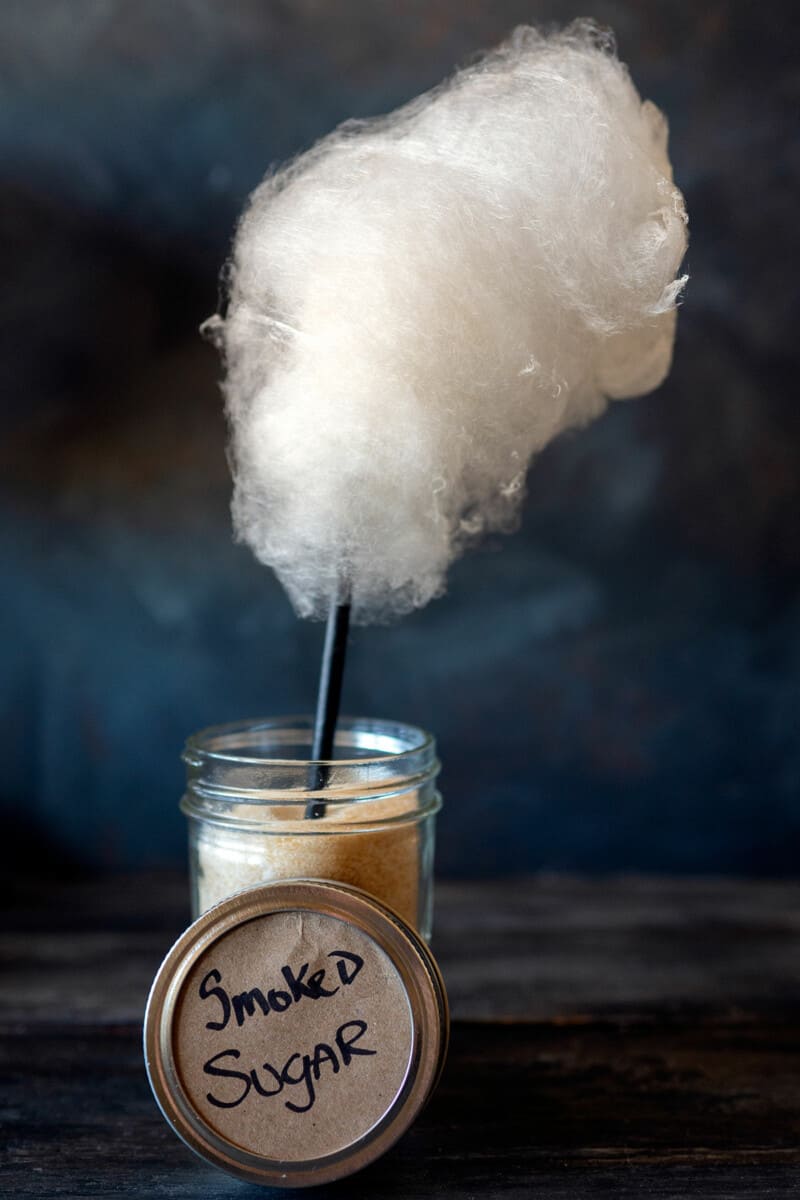 smoked cotton candy on a stick in a jar of smoked sugar.