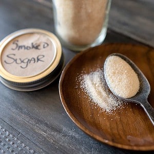 spoonful of smoked sugar next to a jar of smoked sugar.