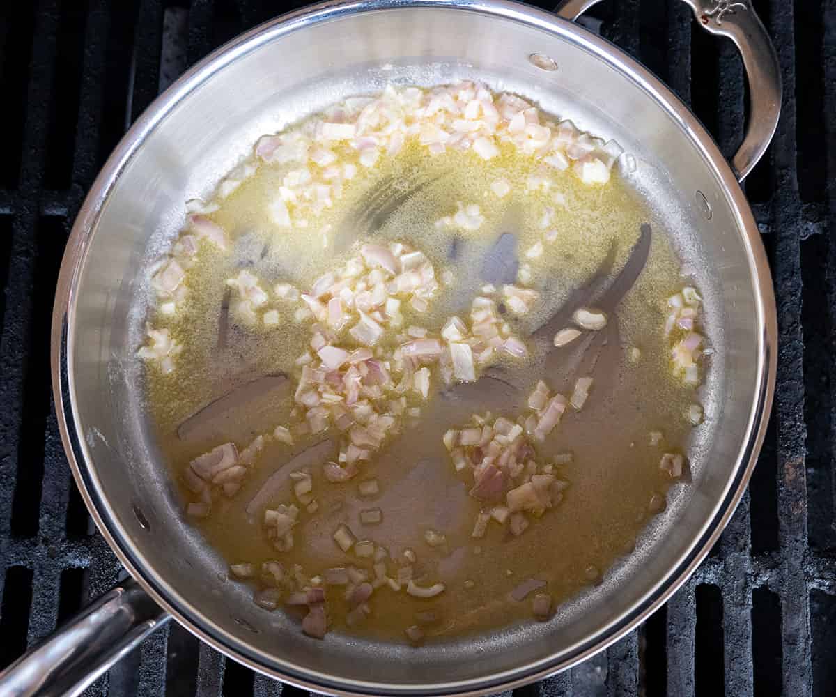 shallots and garlic sauteeing in onions in a skillet on a grill.