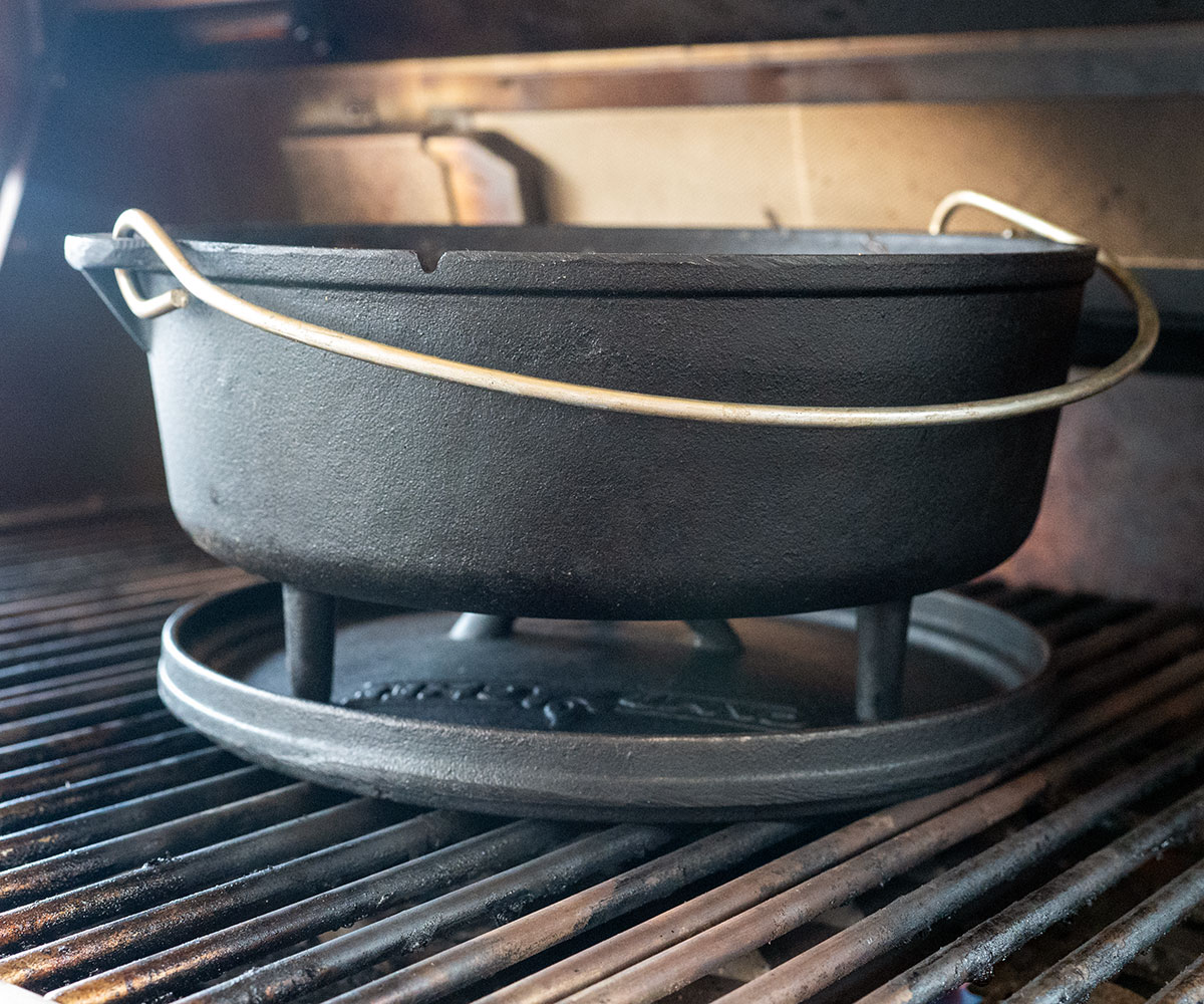 Dutch oven sitting on lid on grill.
