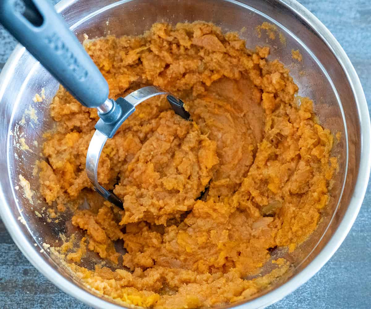 mashing sweet potatoes with a potato masher.