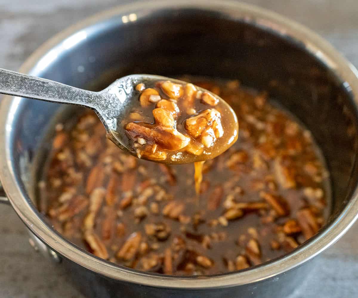 spoon lifting thickened pecan sauce out of pot.