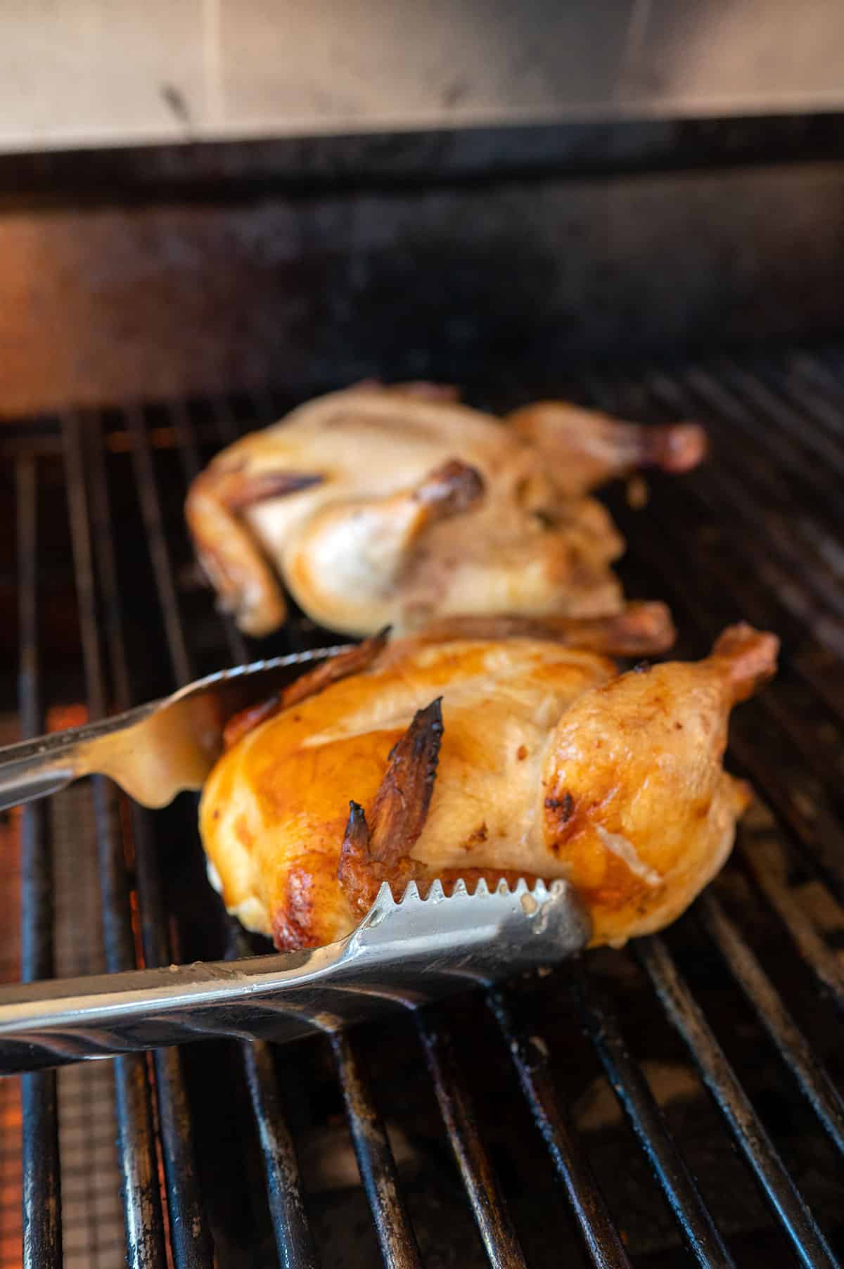 using tongs to rotate cooked cornish hen on grill.