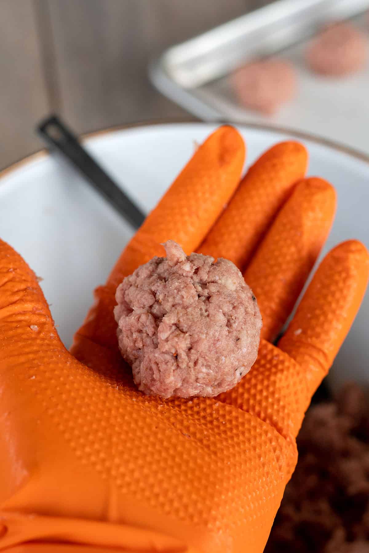 hand with orange glove holding one-inch raw meatball.