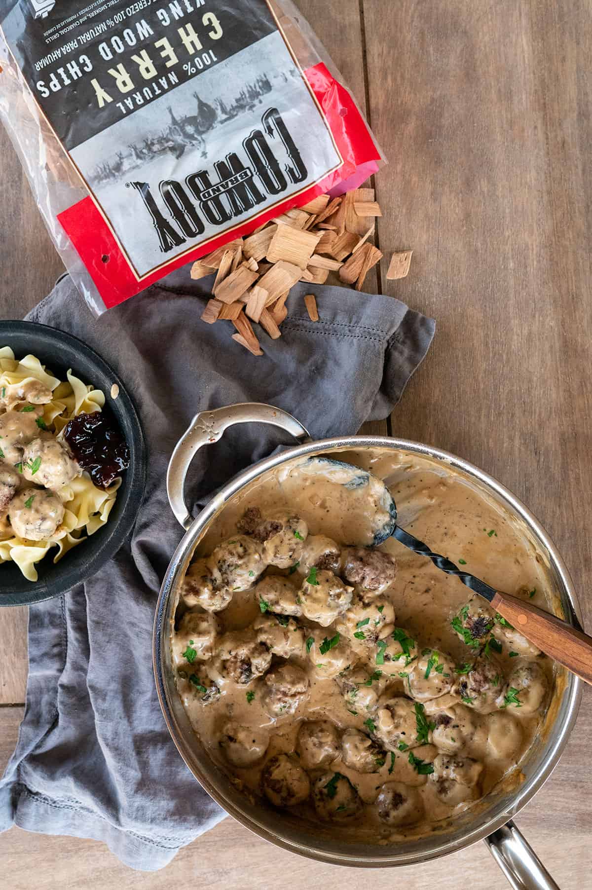 skillet and bowl of Swedish meatballs with bag of Cowboy charcoal wood chips spilled on table.