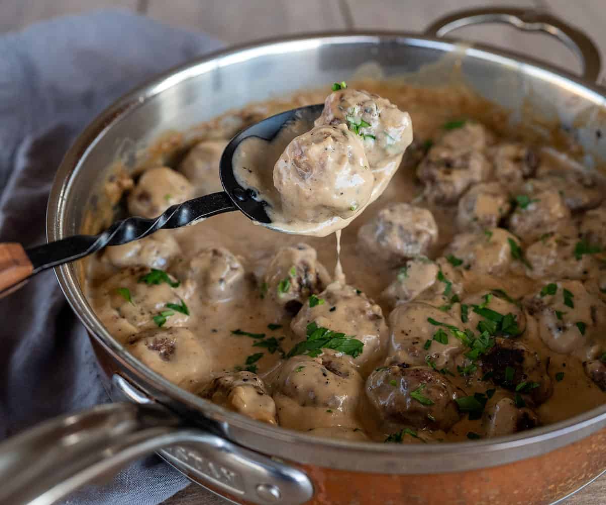Spoonful of two Swedish meatballs and dripping cream sauce.