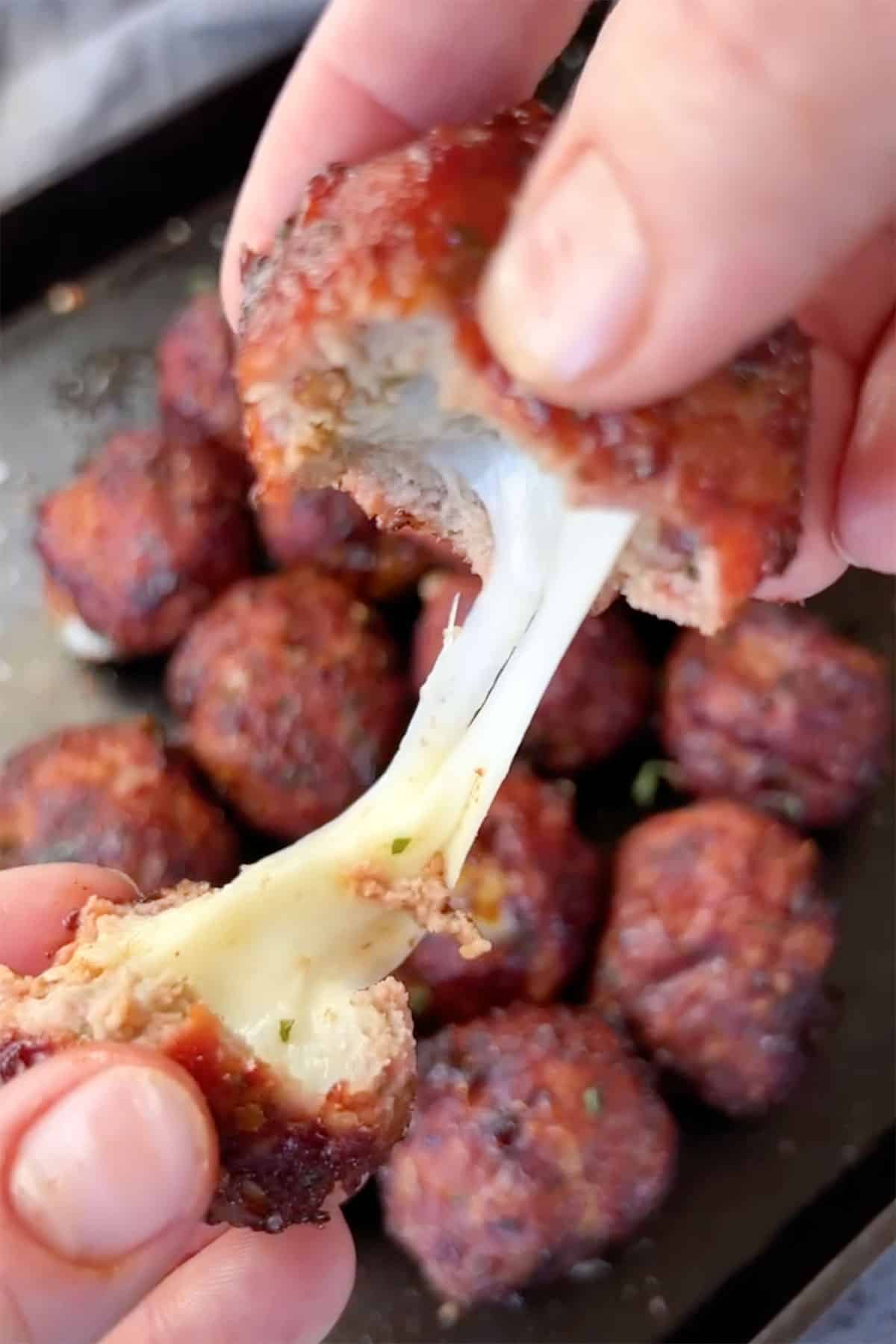 hands pulling meatball apart to reveal cheese.