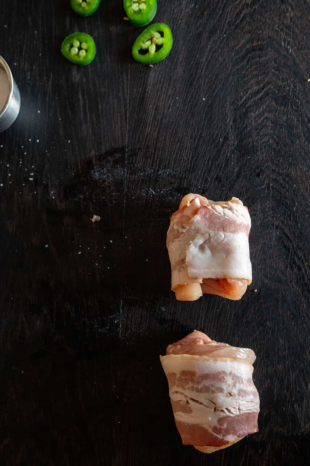 bacon wrapped around chicken thigh on black board.