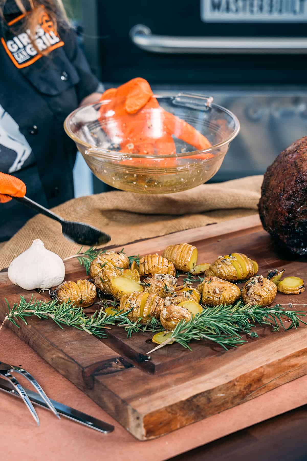 drizzling grilled mini hasselback potatoes with buter.