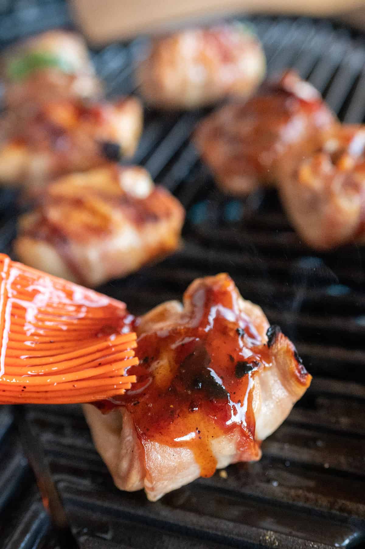 brushing sauce on bacon wrapped chicken thighs.