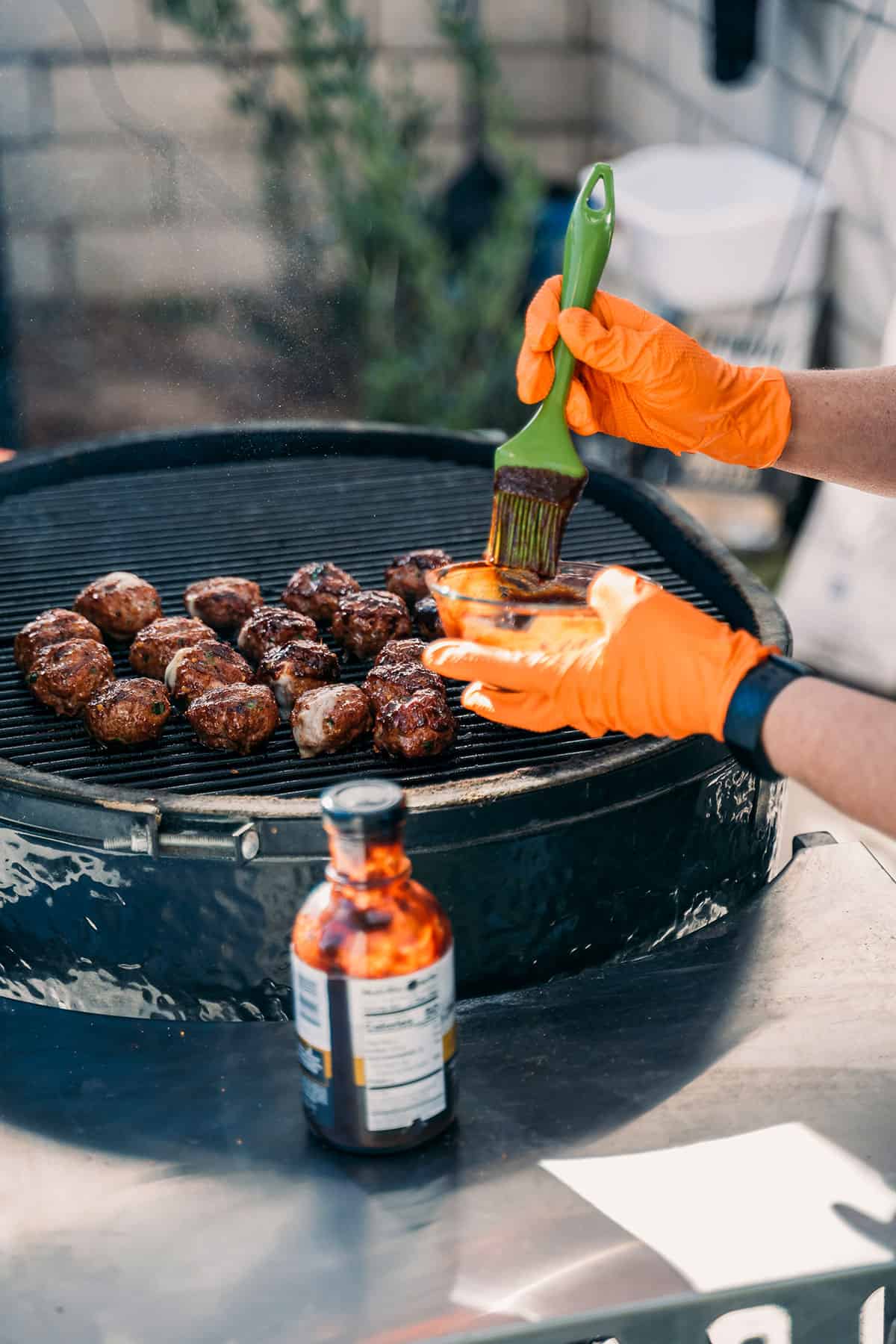 brushing barbecue sauce on meatballs on grill.