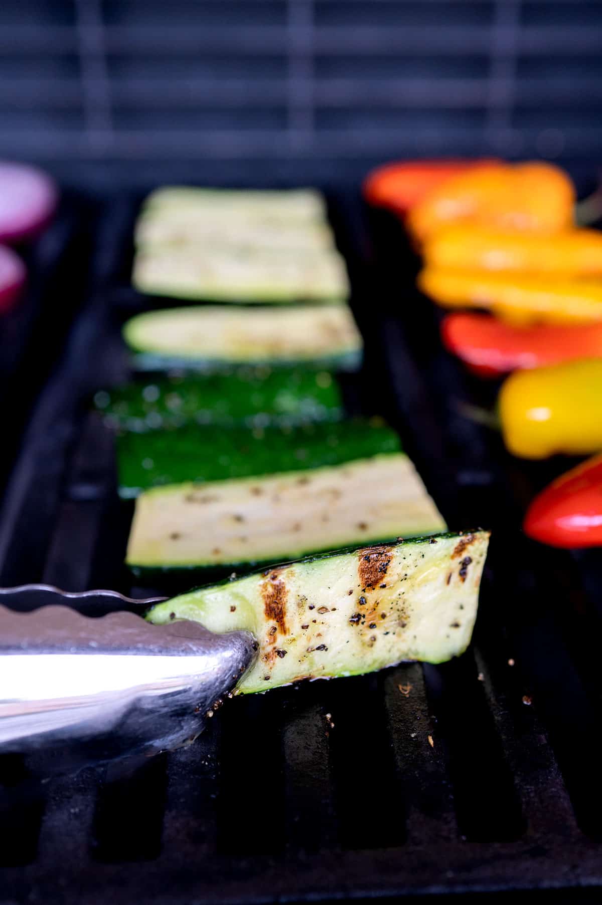 tongs lifting zucchini on grill to reveal grill marks.