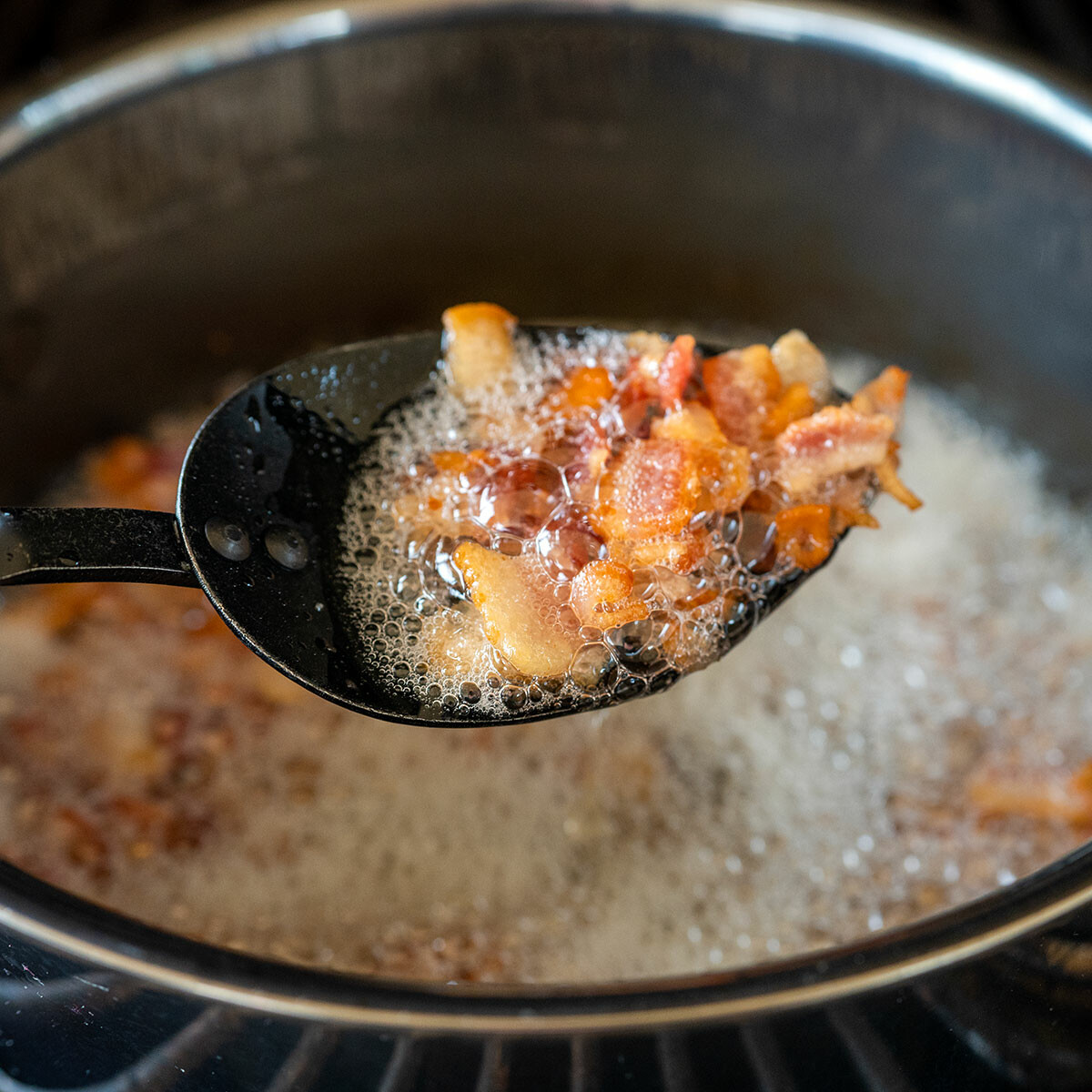 spoon lifting cooked bacon out of a pot.
