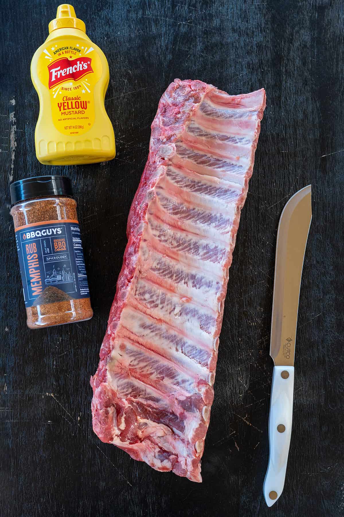 baby back ribs, yellow mustard, barbecue rub and knife.