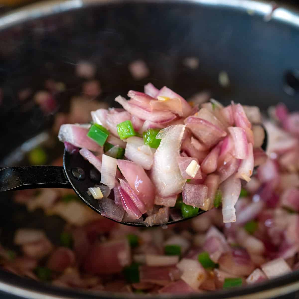 spoon showing sautéed onion, pepper and garlic.