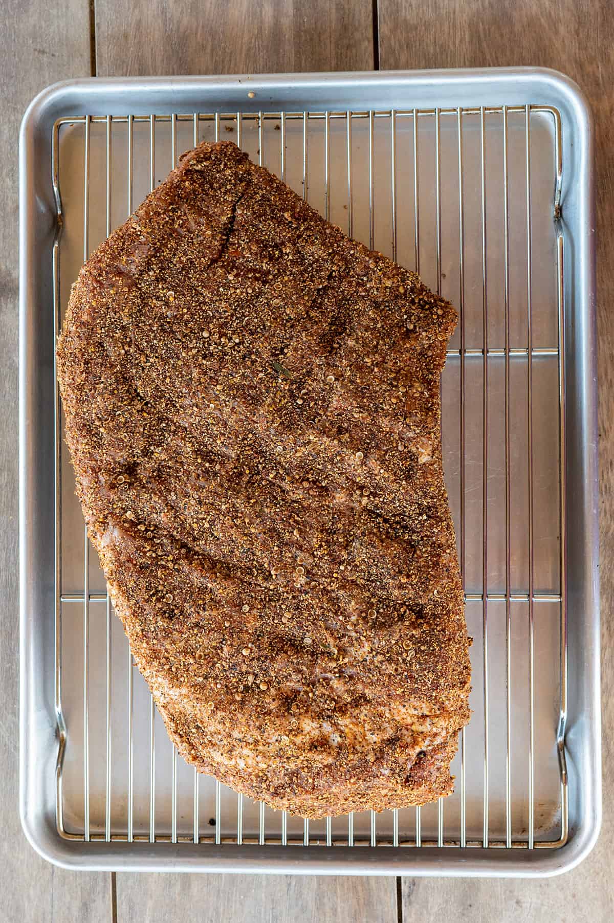 Seasoned raw corned beef brisket on baking rack. 