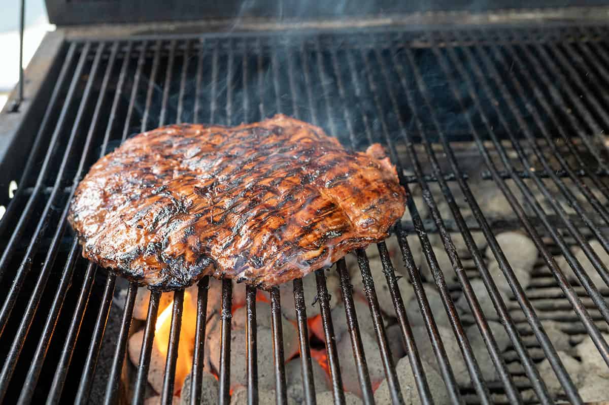 flank steak cooking over charcoal on grill.