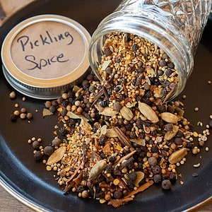 pickling spice spilling out of jar onto black plate.