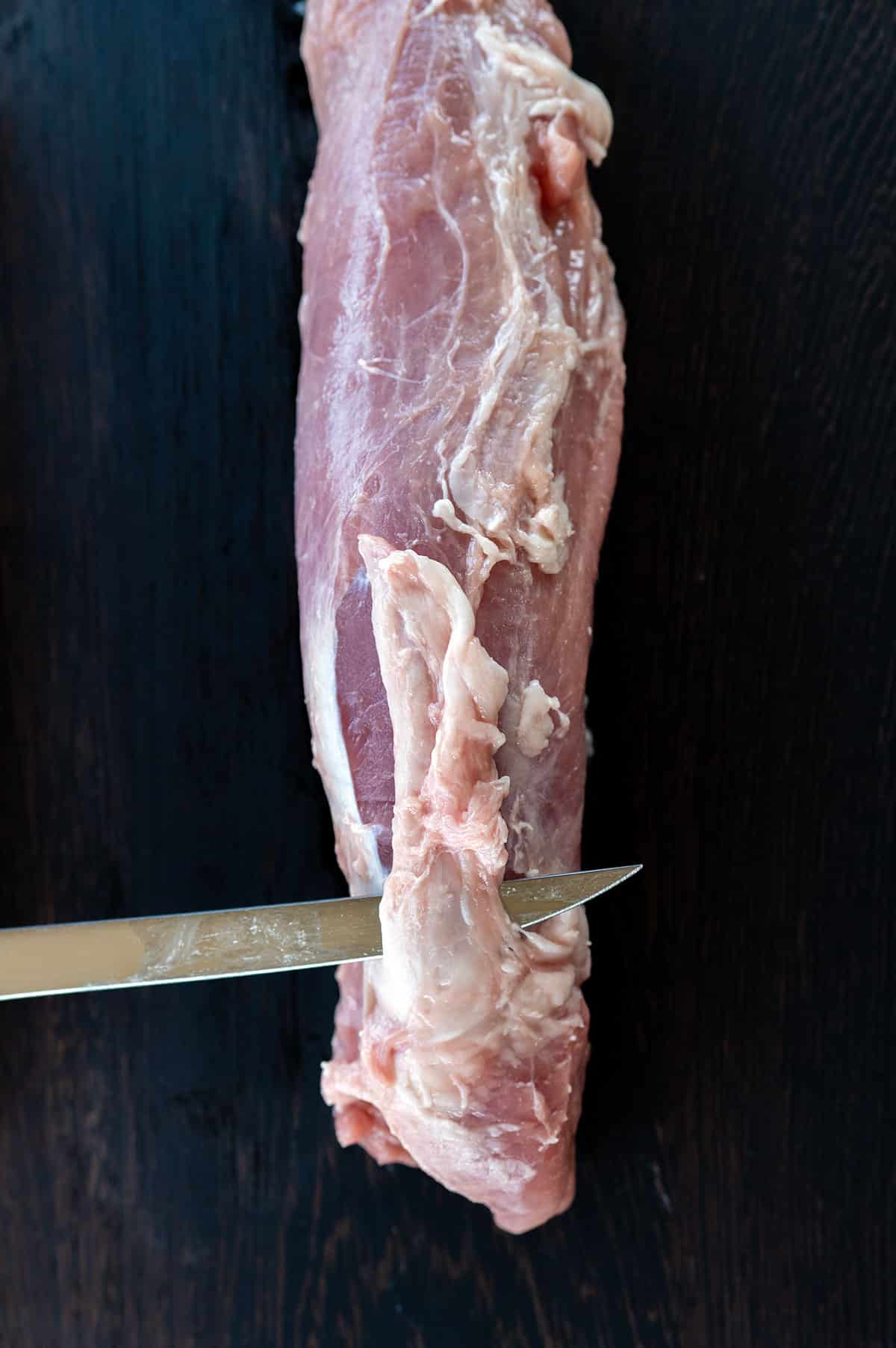 using boning knife to remove silverskin from pork tenderloin.