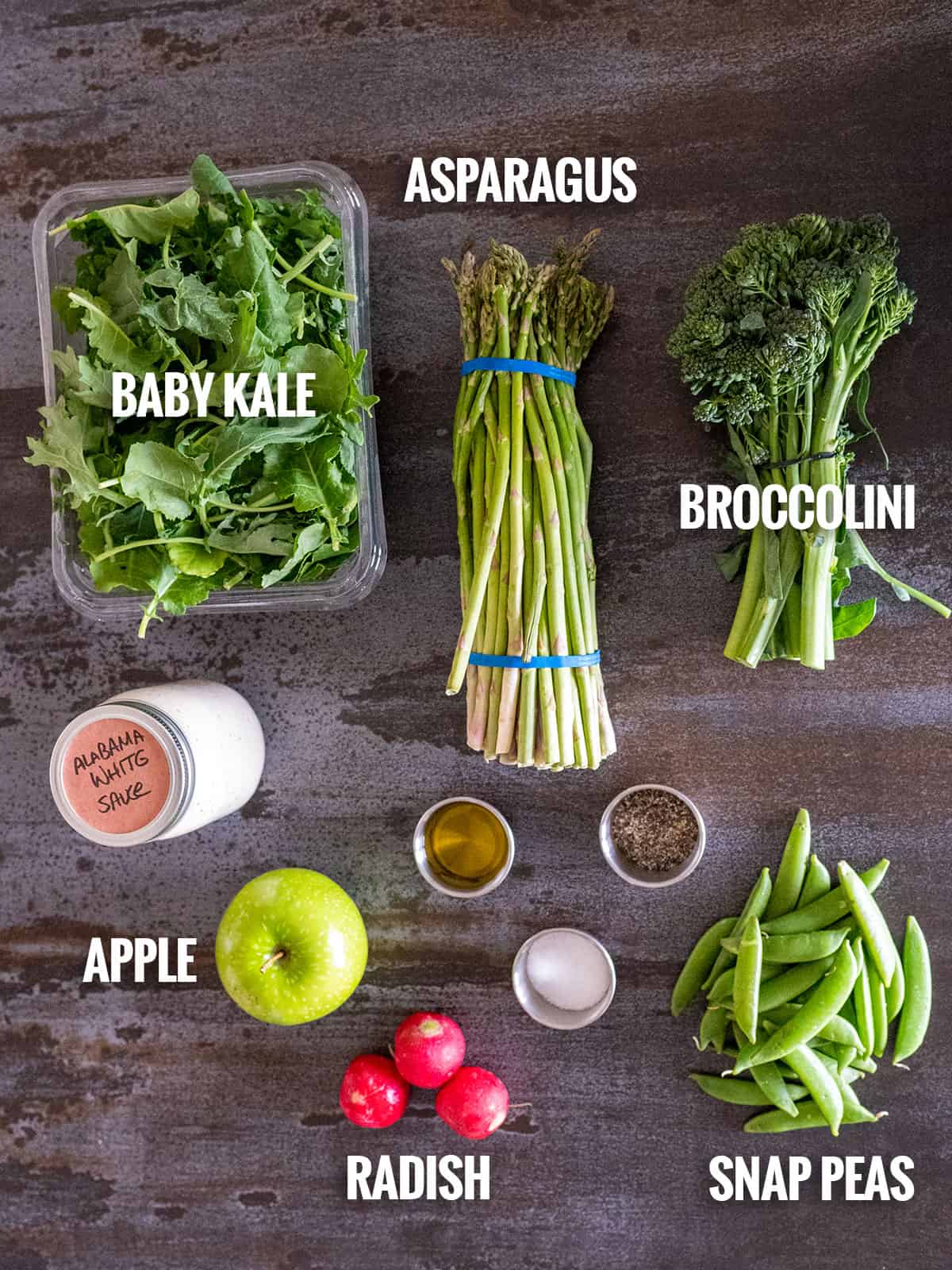 spring salad ingredients: baby kale, asparagus, broccolini, Alabama white sauce, apple, radish, snap peas, salt, pepper, olive oil.