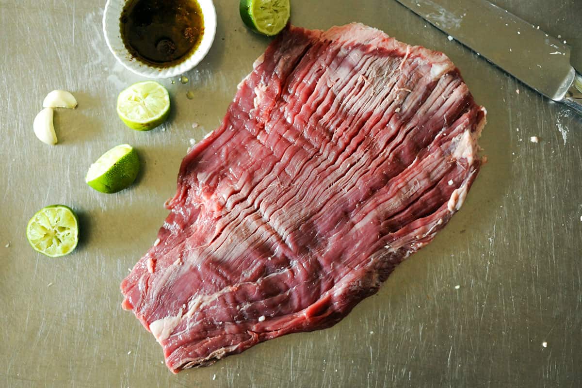 raw flank steak on platter with limes