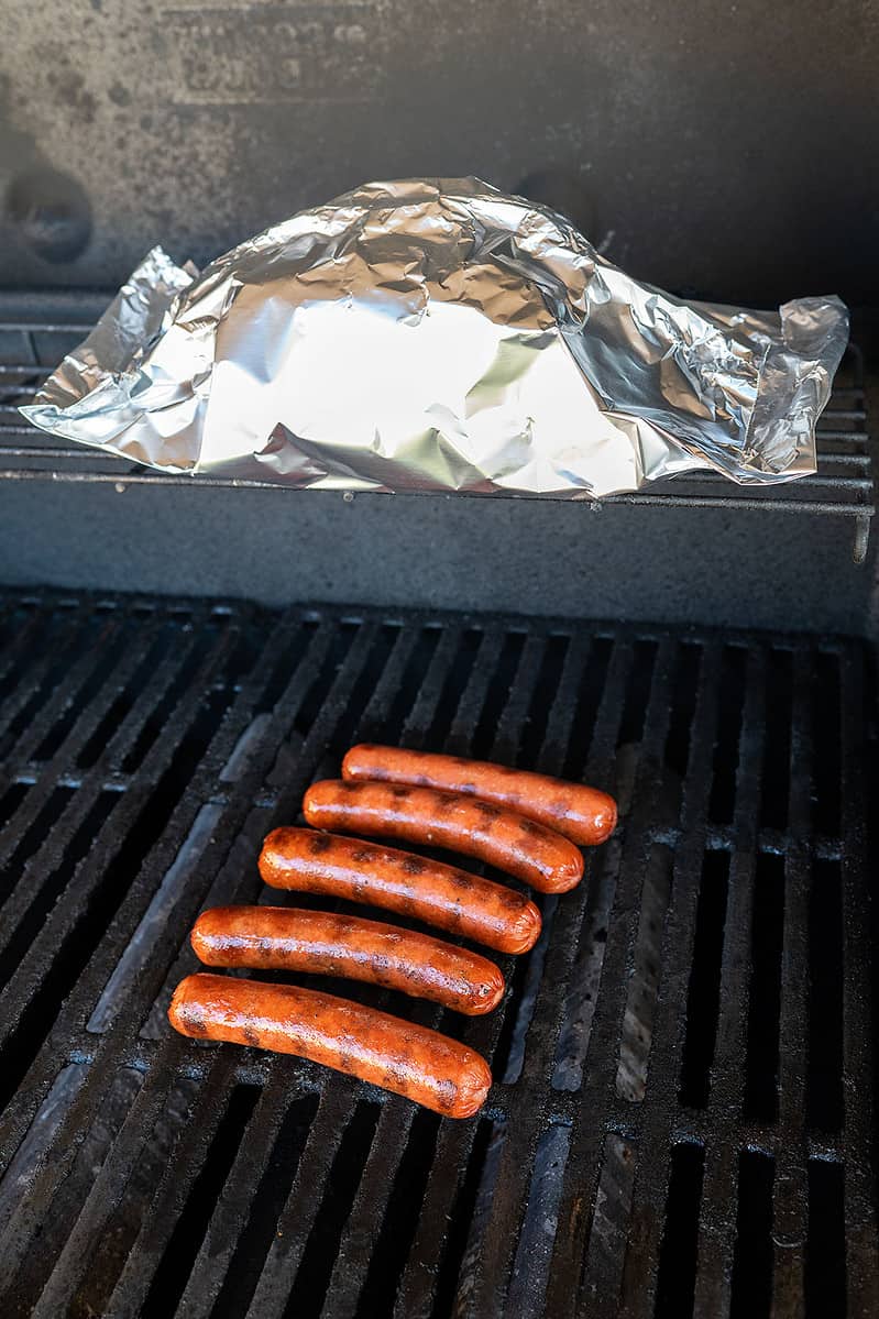 hot dogs on grill with buns wrapped in foil.