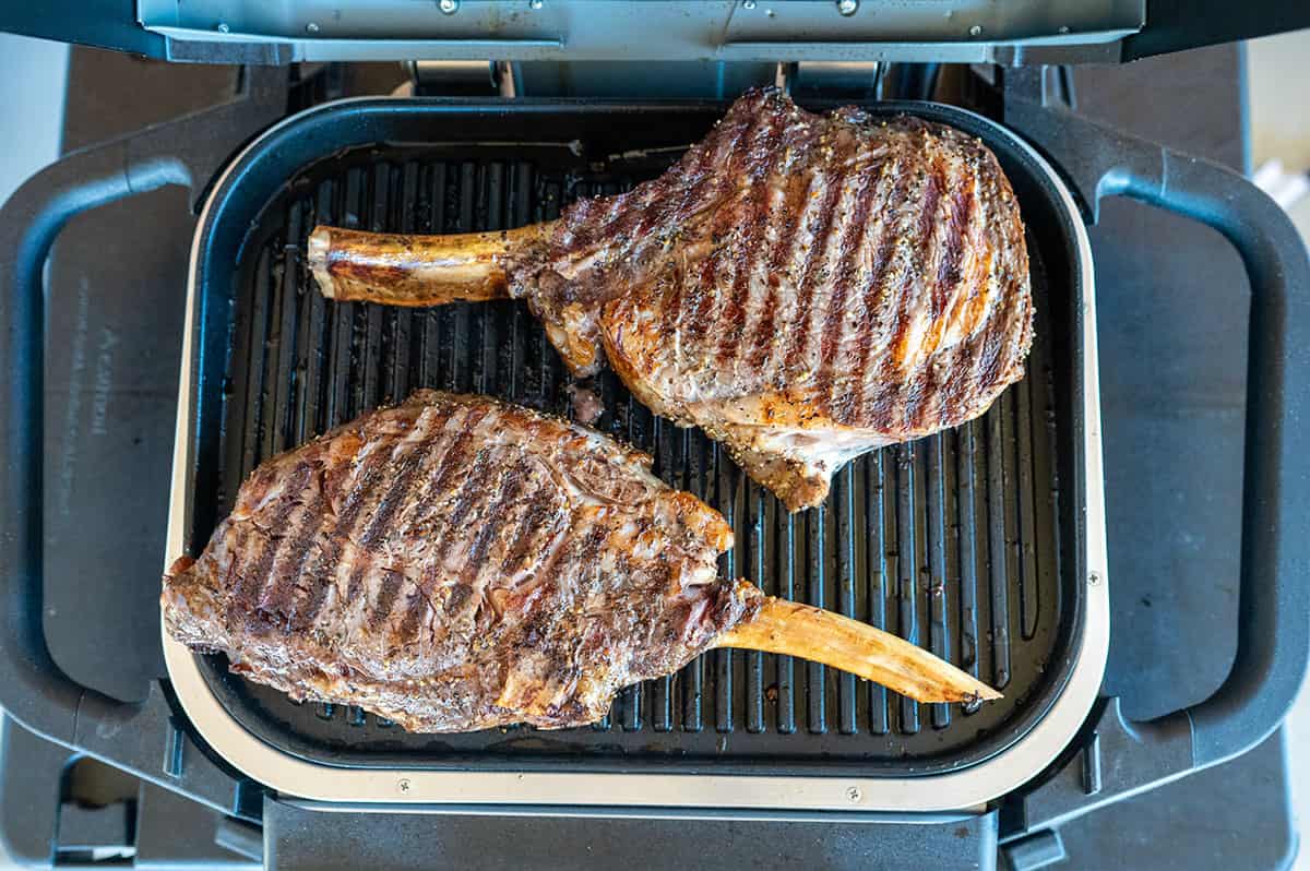 two cowboy ribeye steaks with grill marks on Ninja Woodfire Grill.