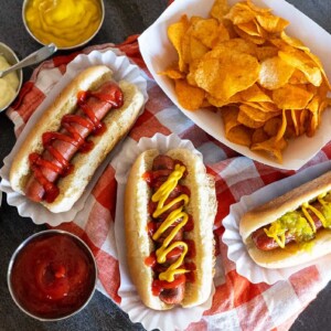 three hot dogs with toppings near bowl of chips.