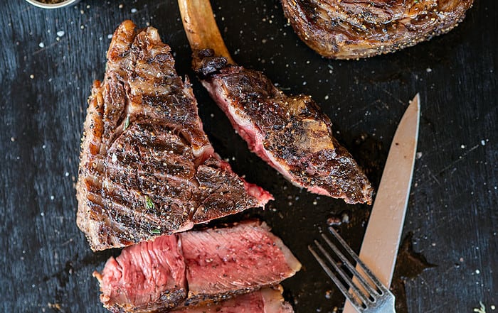 sliced cowboy ribeye steak on black platter.