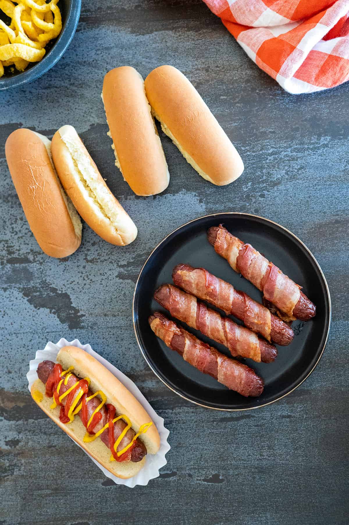 4 bacon-wrapped hot dogs on plate, 1 on bun. 
