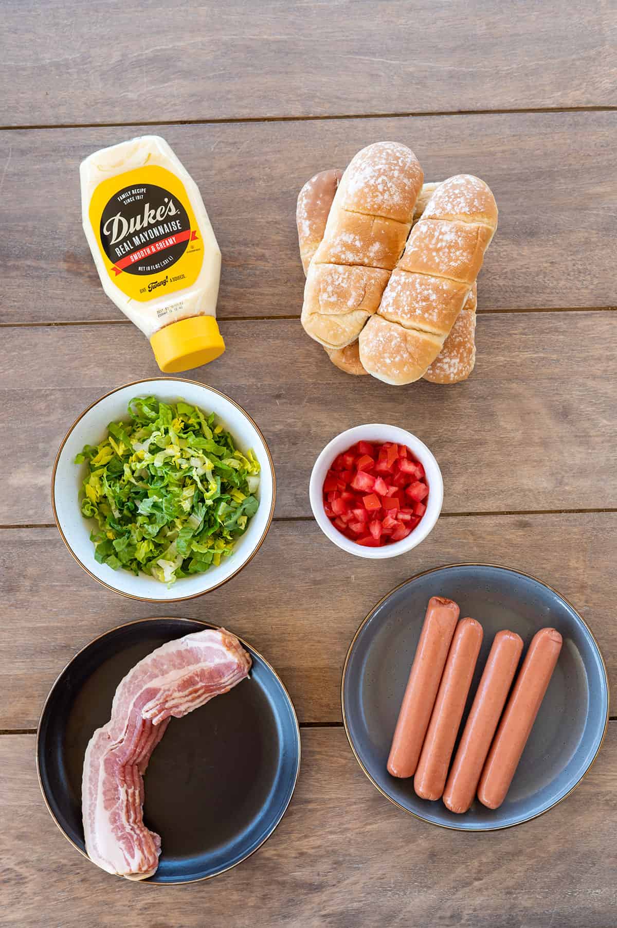 ingredients for BLT hot dogs: mayo, buns, lettuce, tomatoes, bacon, hot dogs.