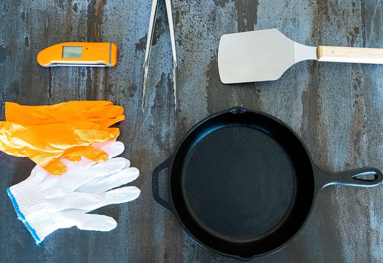 grill tools on table: gloves, thermapen, spatula, tongs, cast iron