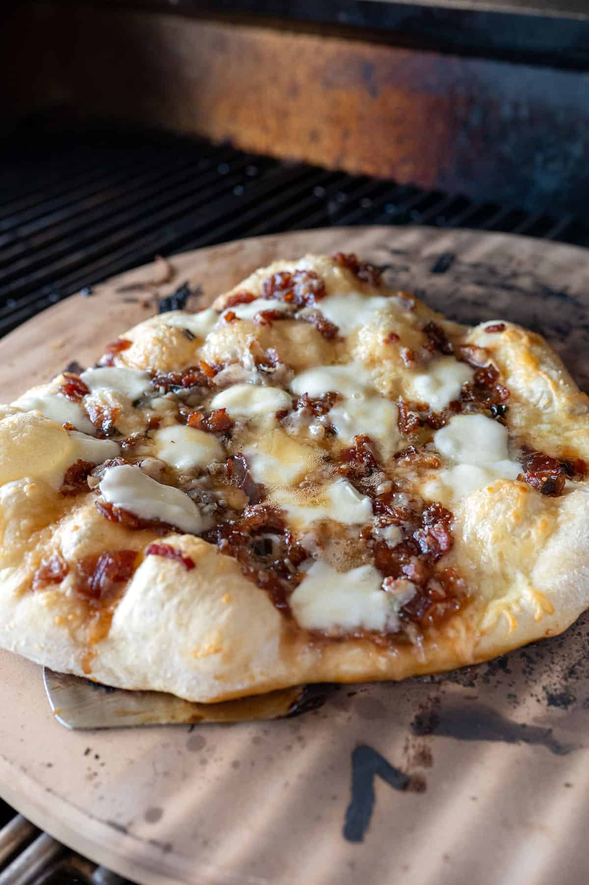 close up of bacon jam pizza on baking stone on grill.