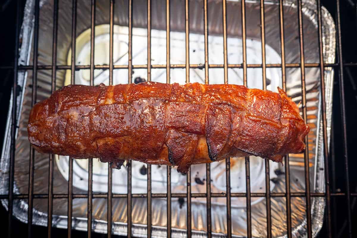 bacon-wrapped pork tenderloin getting crispy on grill.