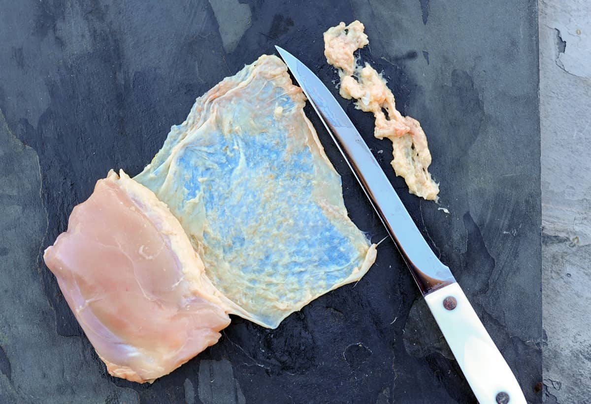 using knife to scrape fat from chicken thigh skin.