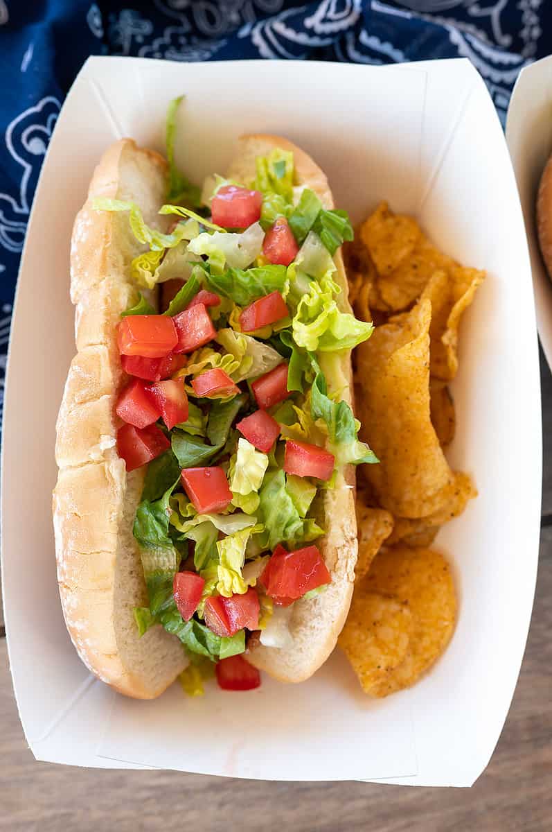 bacon-wrapped hot dog topped with lettuce and tomato.