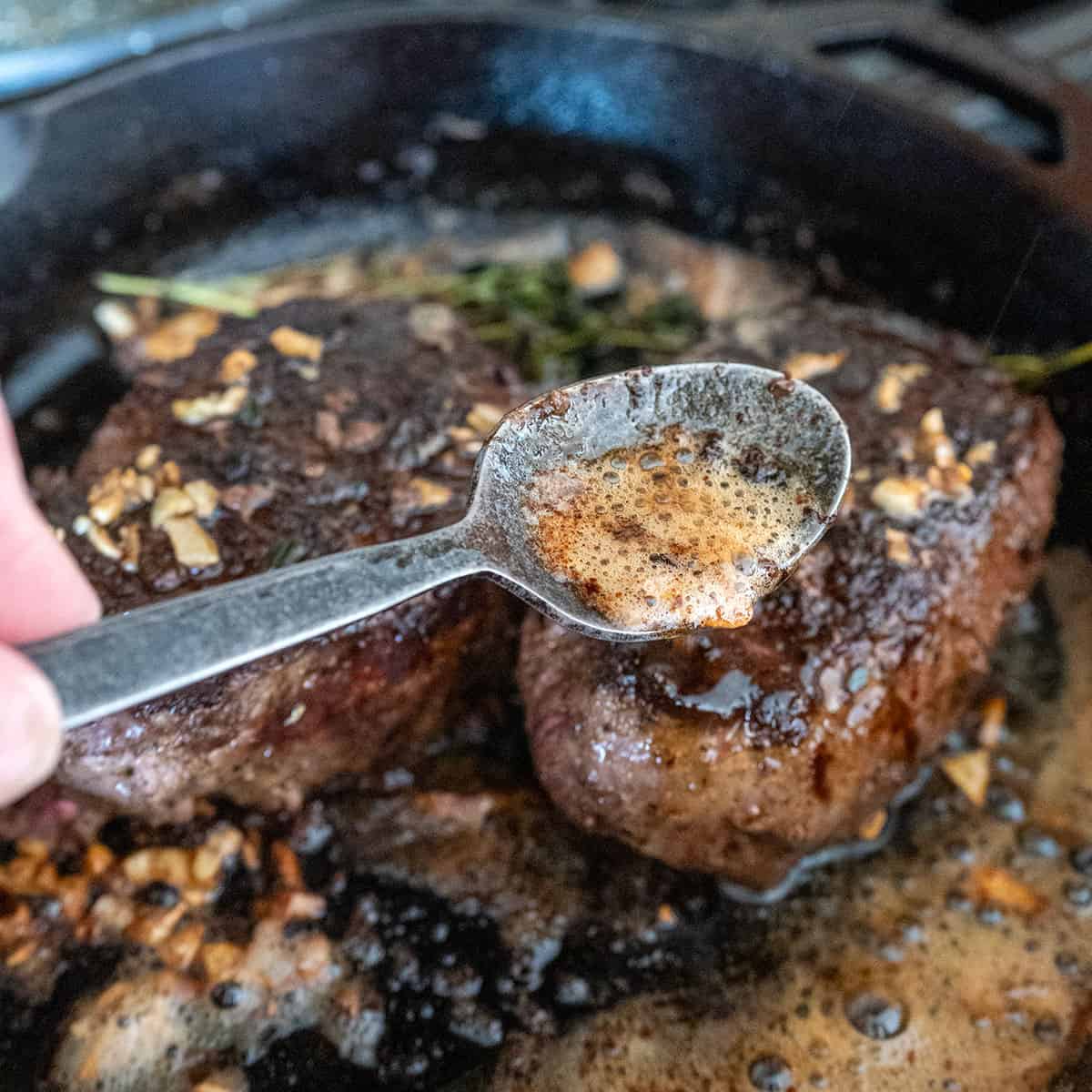 Basting garlic herb butter onto steak in pan.