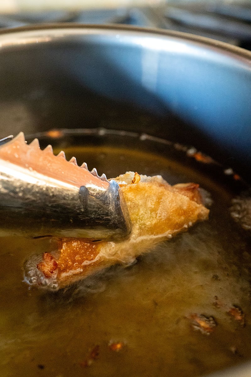 tongs holding a cooked lumpia taco in oil.
