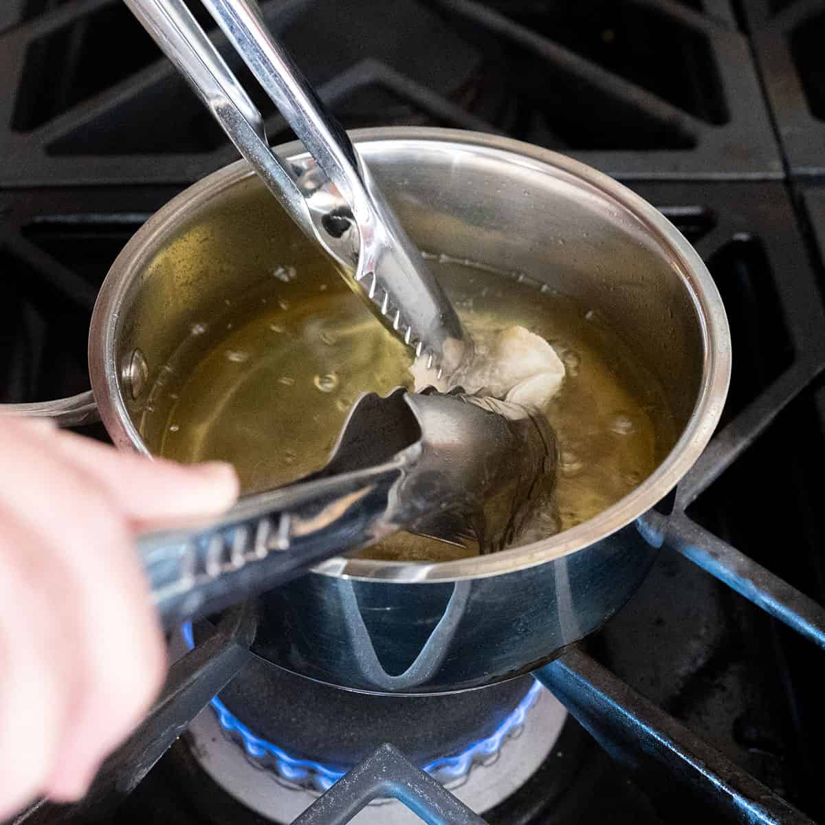Two pairs of tongs holding lumpia taco shell in oil.