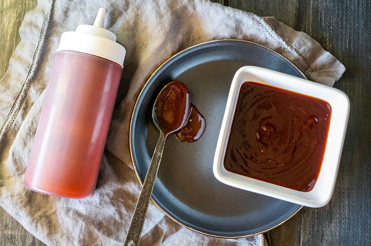 BBQ sauce in a bowl and bottle with spoon.