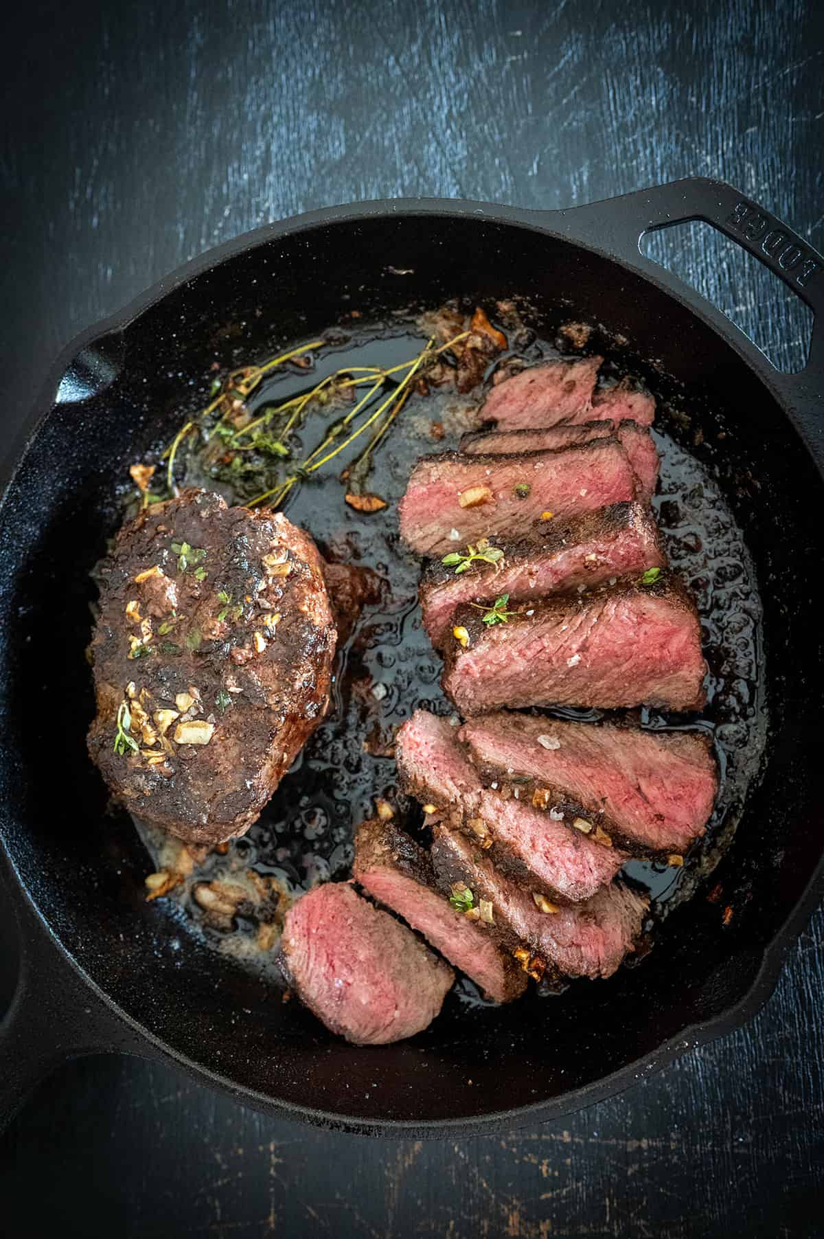 Medium-rare slices of steak in cast iron skillet with herb butter. 
