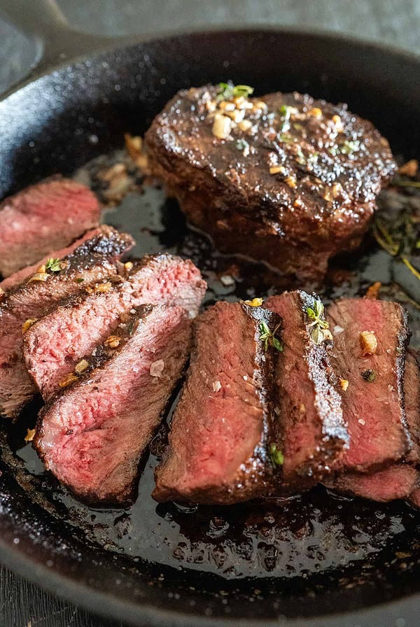 Medium-rare slices of steak in cast iron skillet with herb butter.