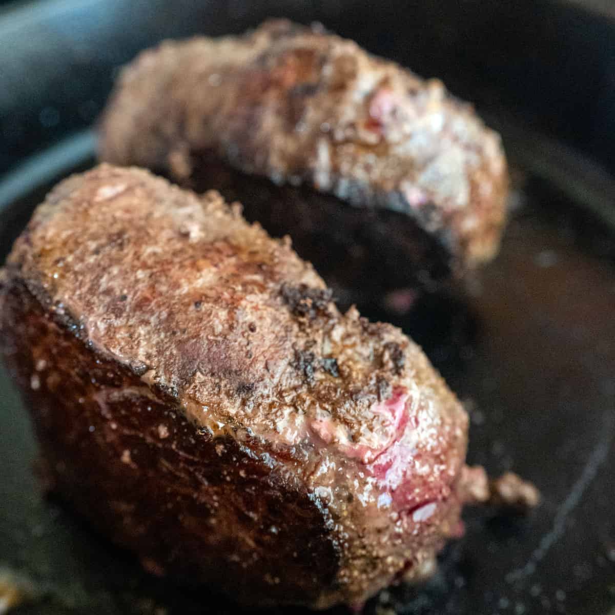 Steaks cooking on their sides in a cast iron pan.
