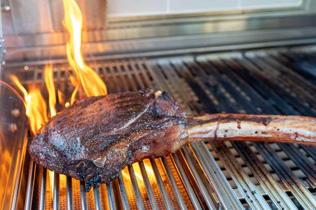 tomahawk steak on gas grill getting seared with flames.