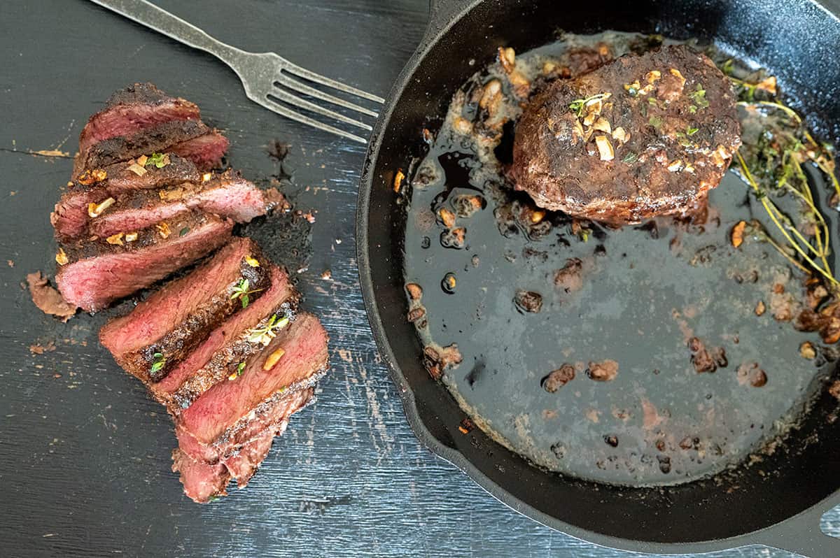 one sliced steak on cutting board. One in pan. 
