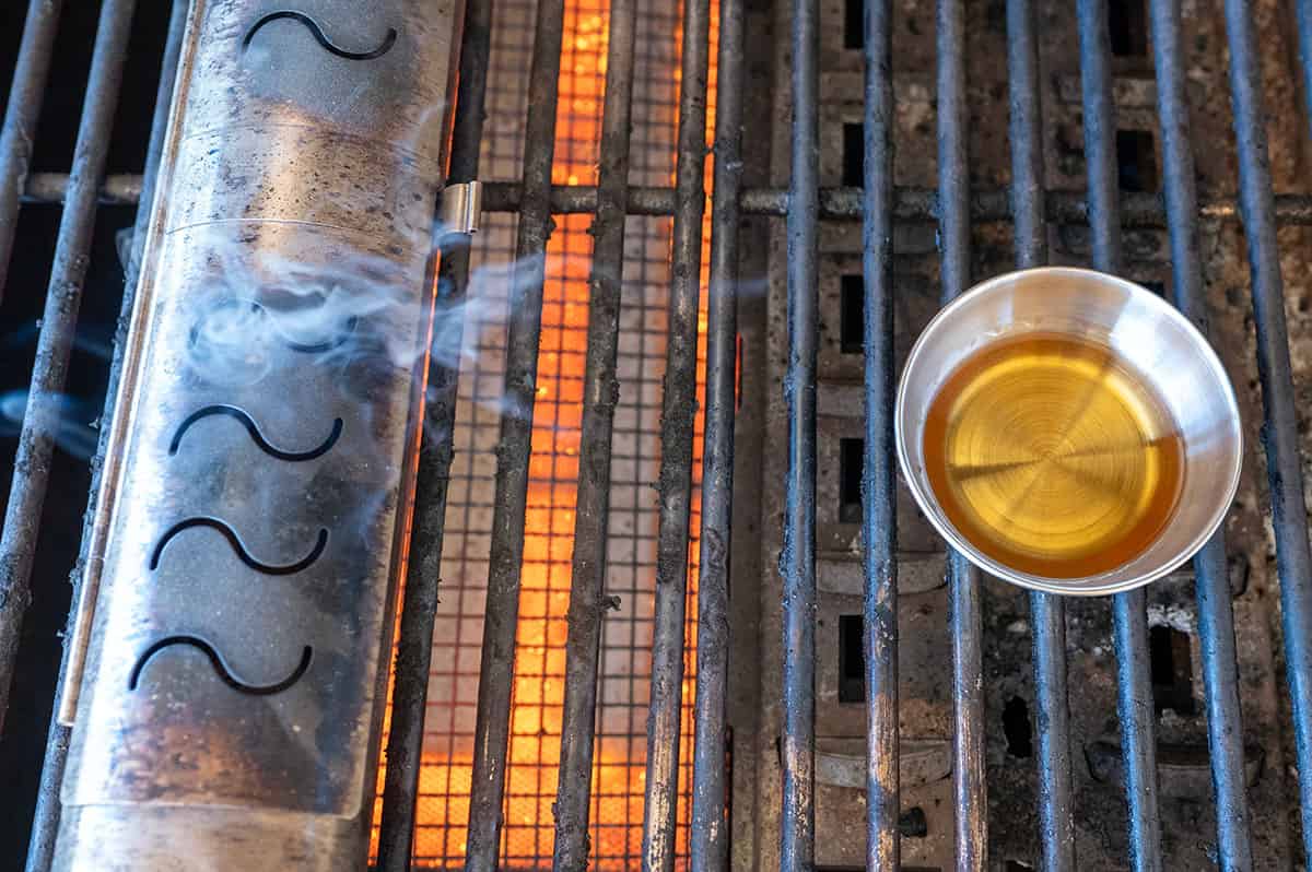 Bowl of whiskey next to smoke on grill.