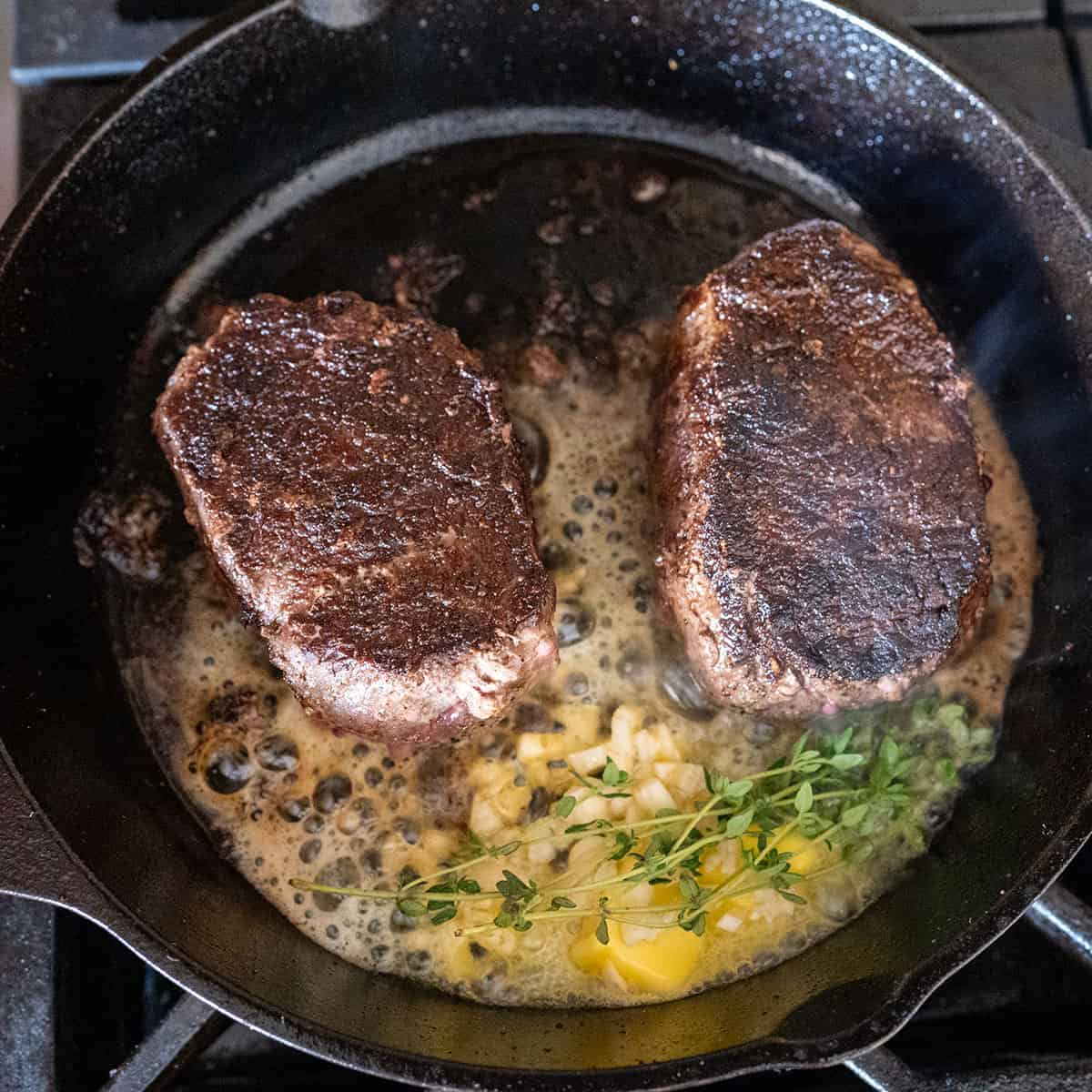 two seared steak in a pan with butter, garlic and herbs.